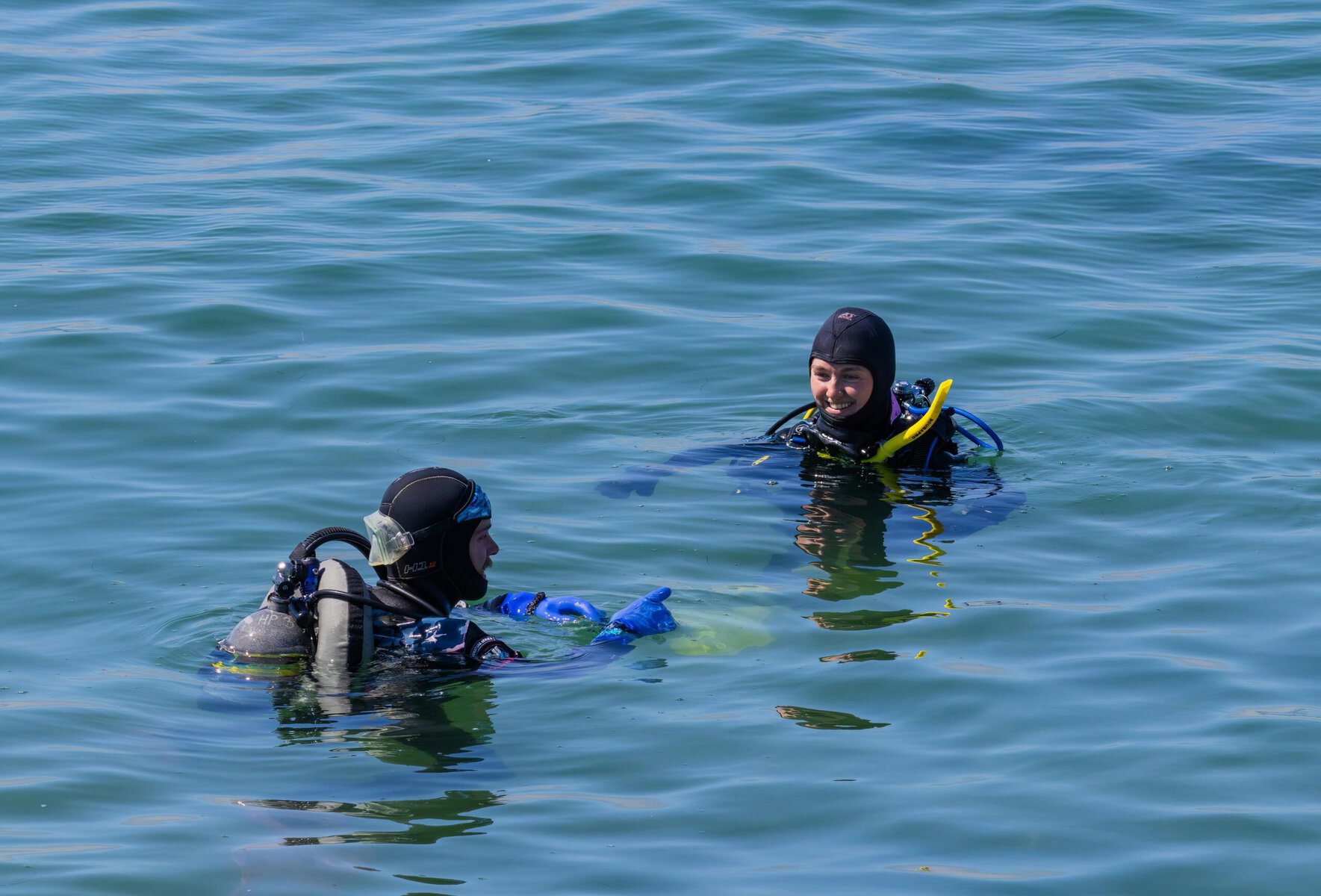 Two scuba divers enjoying a sunny day in clear open water, equipped with full scuba gear.